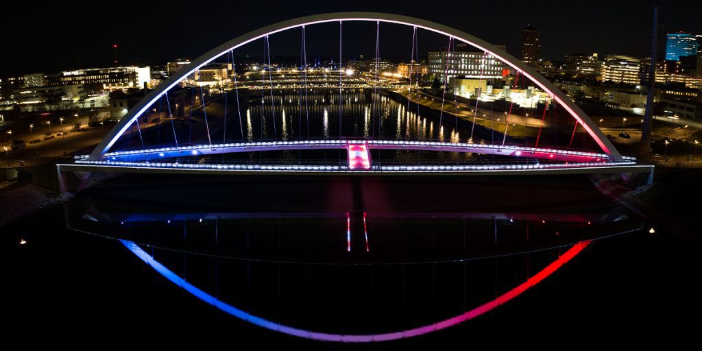 The Iowa Women of Achievement Bridge lit with Musco color-changing LED lights reflected in the Des Moines River