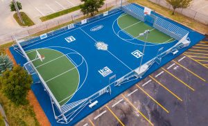 Basketball mini-pitch with blue and green court surface and white logos..