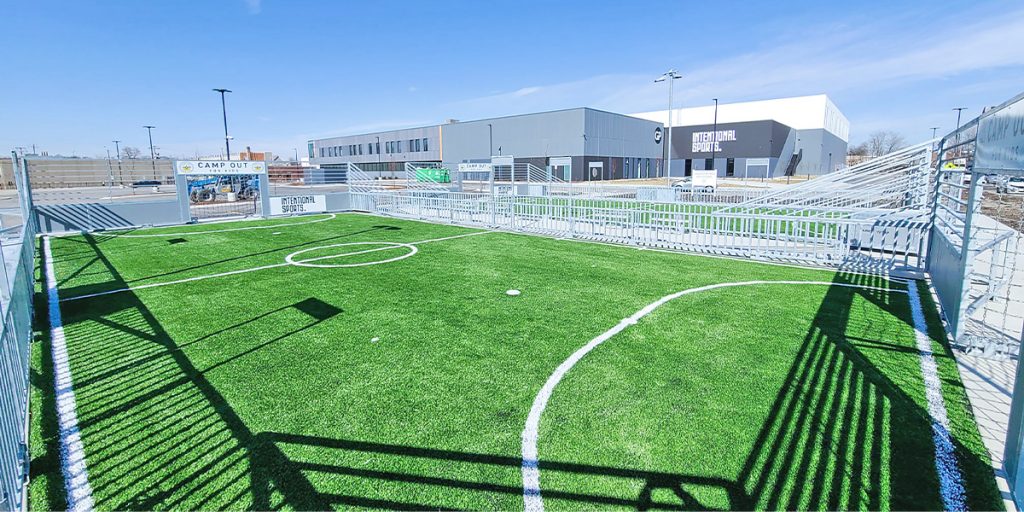 Musco Mini-Pitch system with turf surface and Intentional Sports campus in the background.