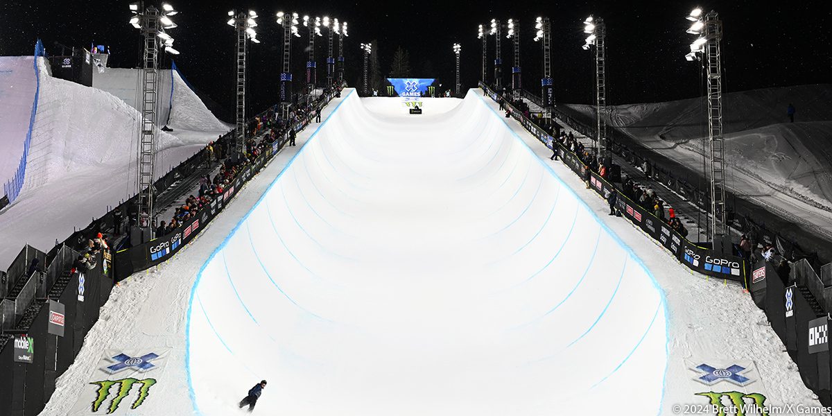 Skiier finishes night run on X Games Superpipe at 2024 winter games in Aspen, A row of Musco LED temporary lighting lines the Superpipe on either side.