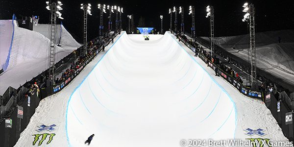 Snowboarder finishes night run on X Games Superpipe at 2024 winter games in Aspen, A row of Musco LED temporary lighting lines the Superpipe on either side.