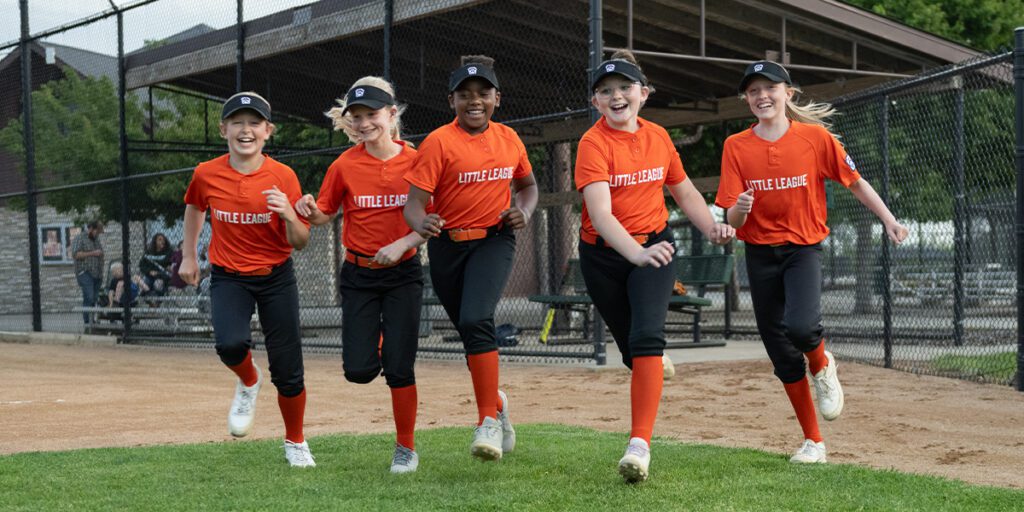 Girls on Little League softball team running onto the field.