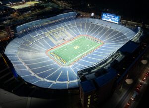 Overhead view of University of Michigan's Michigan Stadium stands and football field lit at night.
