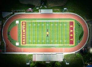 Overhead view of Hazelwood East High School football field in red and gold school colors lit at night.