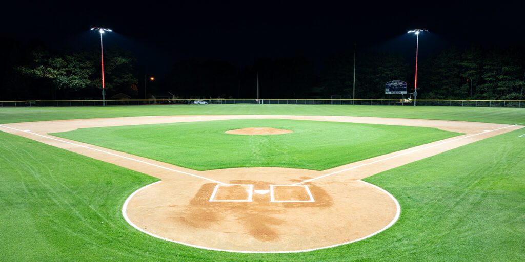 Lakeman field viewed from behind home plate. As part of the fan experience, red accent lighting shines up the two poles and led fixtures in the background.