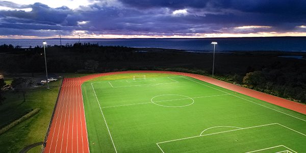 Universite Sainte-Anne lights DarkSky certified soccer field while the sunsets behind mountains in the background.